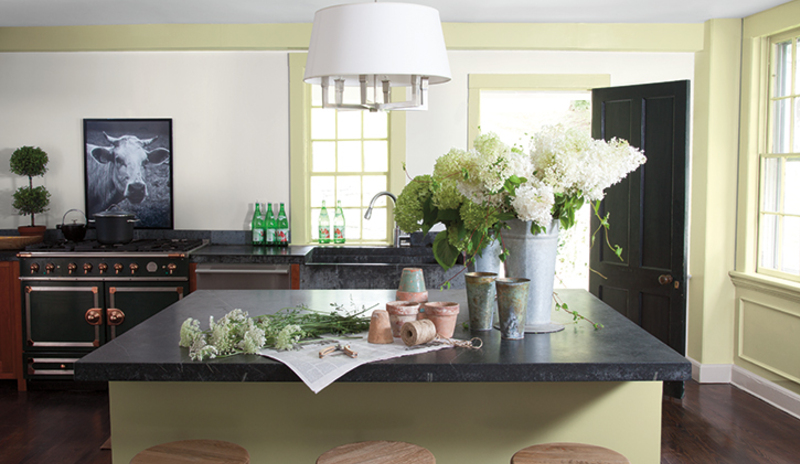 A modern green-painted kitchen with cut flowers and granite countertops.