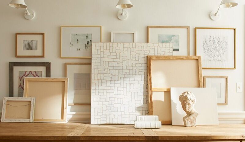 Fresh white gallery wall with pink undertone, wooden console table, art frames, and off-white sconce
