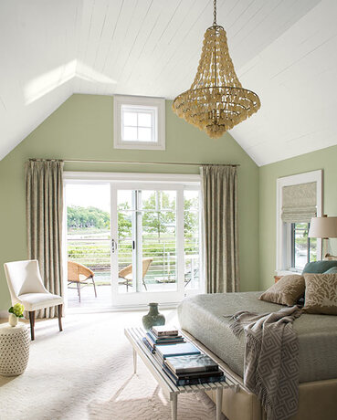 A light green-painted master bedroom with chandelier and glass sliding doors leading to outside deck