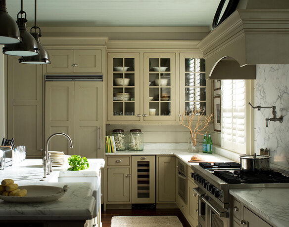 A country style kitchen with green-gray painted cabinets and marble countertops.