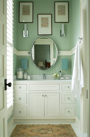 A green-painted bathroom with white built in sink cabinets and marble countertop.
