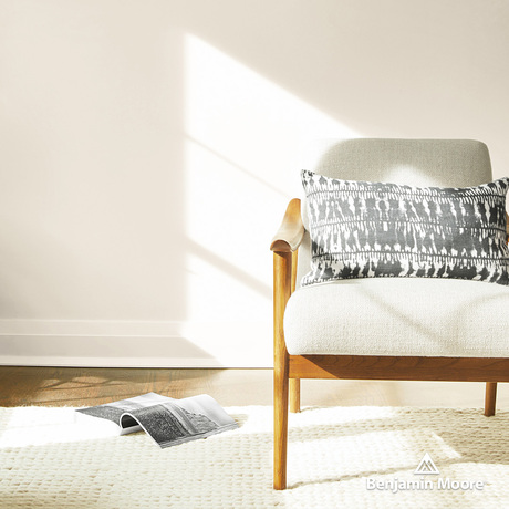A sunlit sitting area with an off-white painted wall and wood-framed armchair