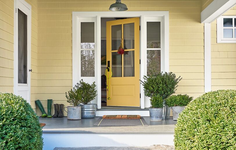 The front porch of a yellow-painted house with a yellow door, white trim, plants in metal pails, The front porch of a yellow-painted house with a yellow door, white trim, plants in metal pails,